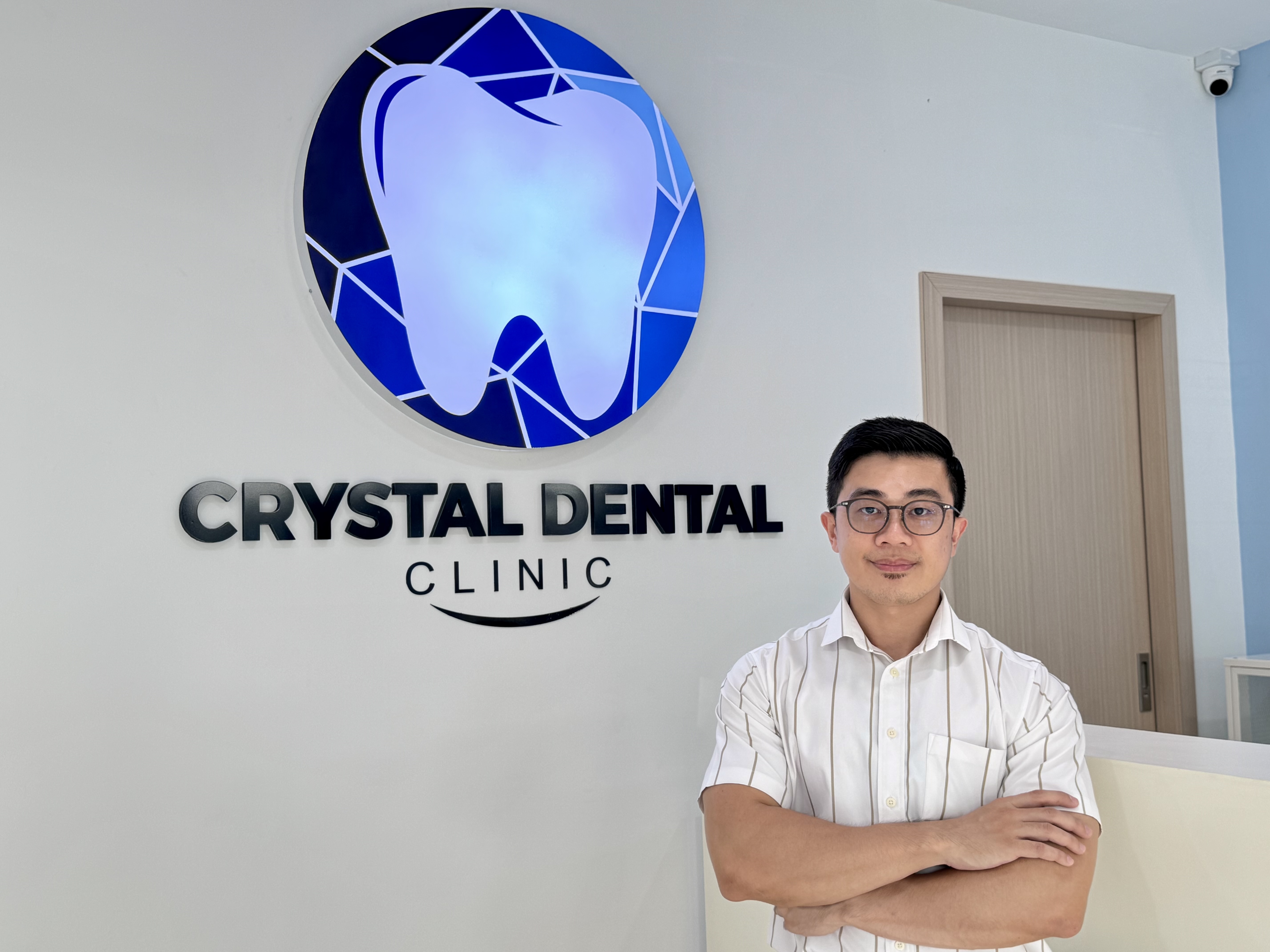 Crystal Dental doctor standing by clinic logo